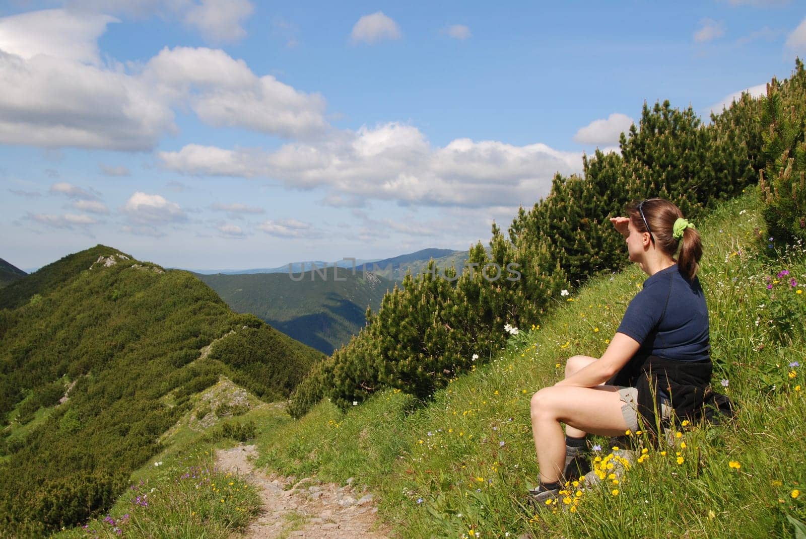 Hiking woman siting in grass and looks to mountains