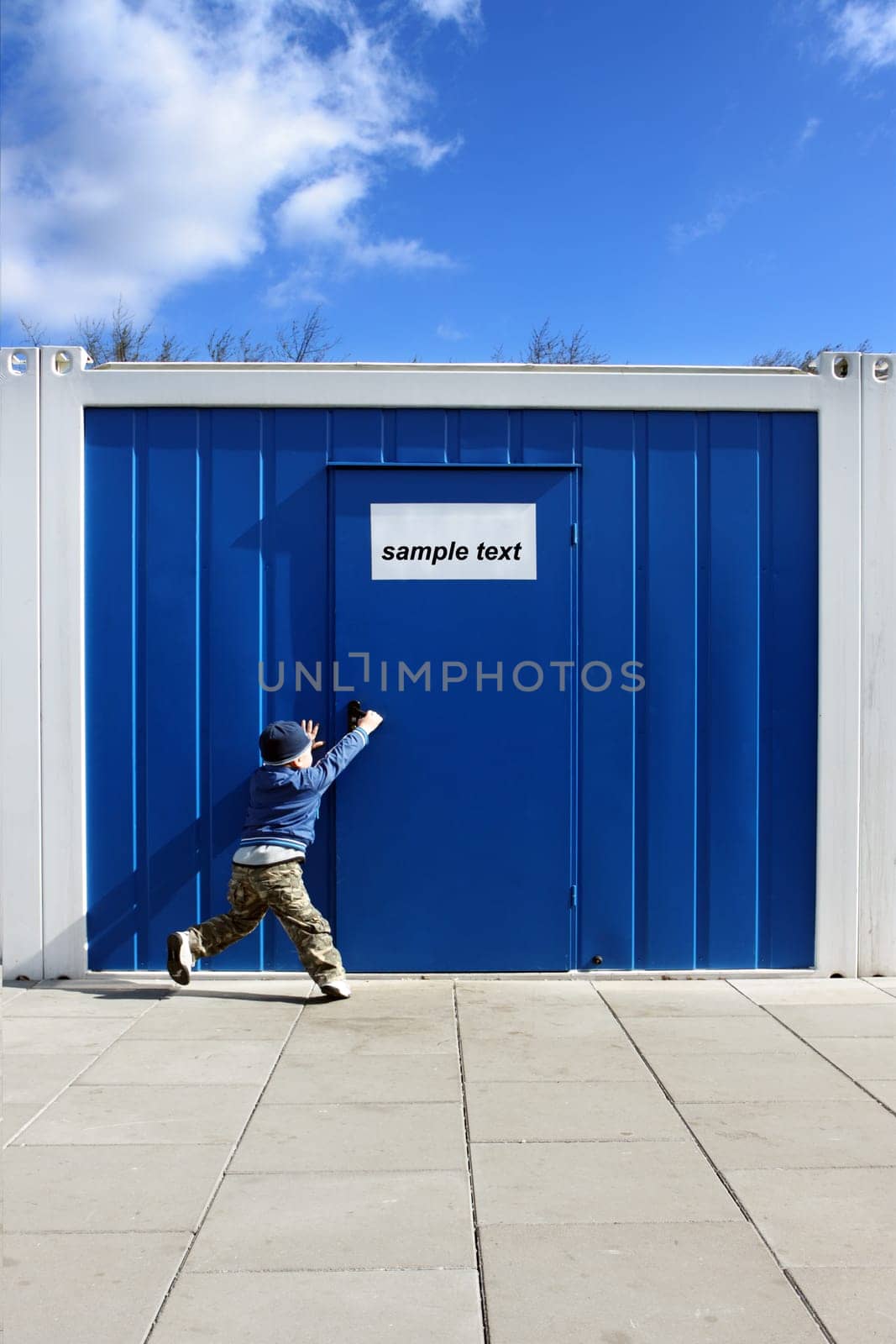 Baby boy wants to open the door handle near blue cellular homes.