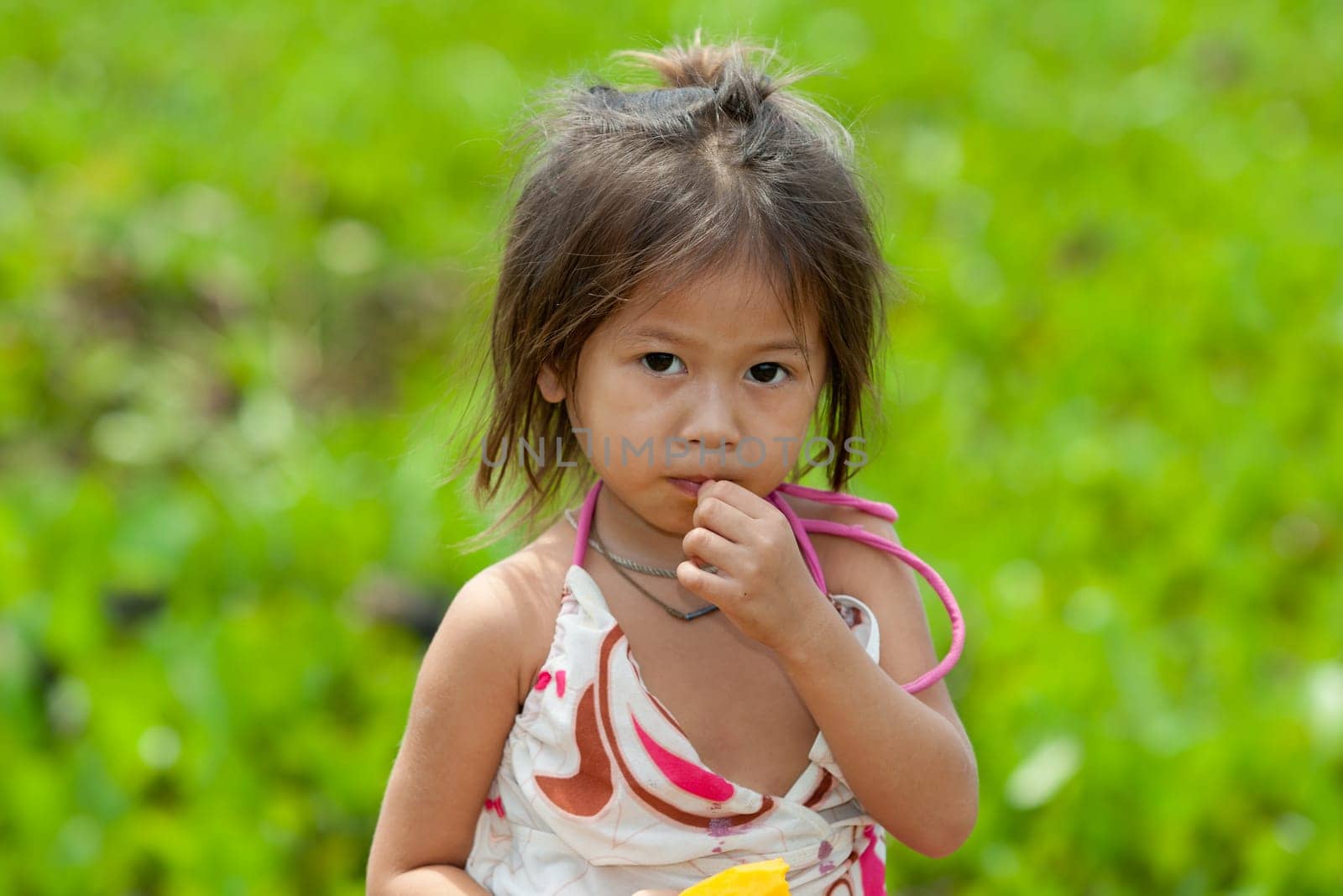Portrait of girl from Asia,child in poor clothes eating mango