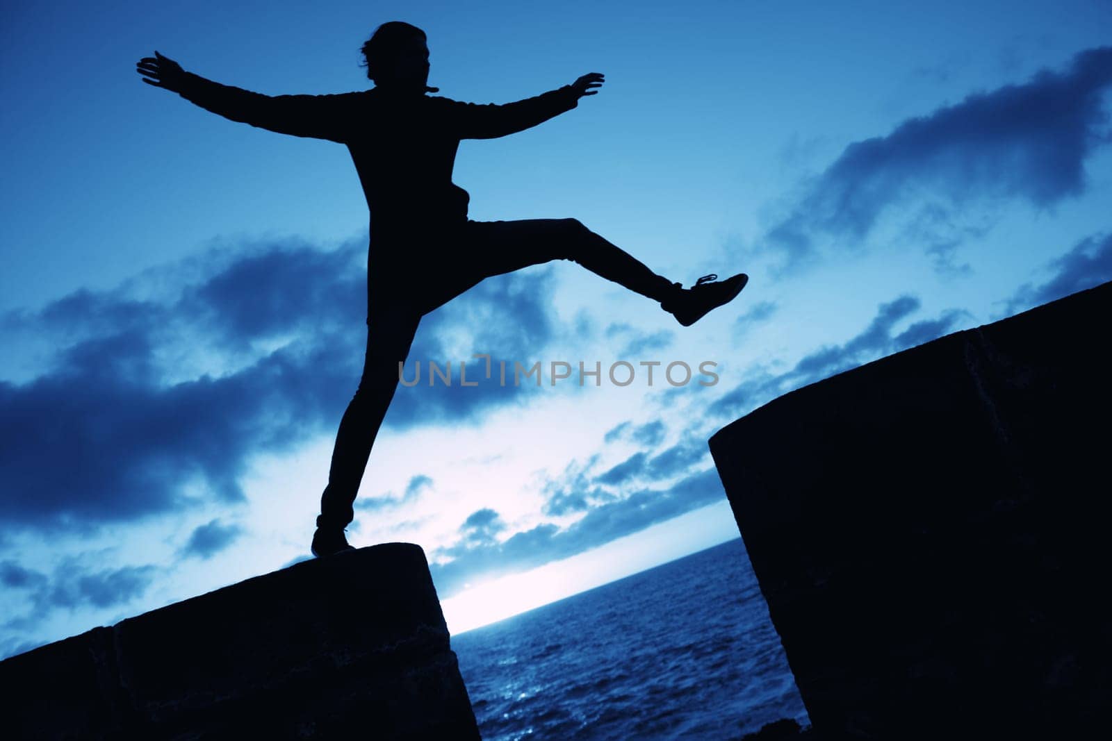 Silhouette of a woman jumping into the air on a wall, against blue cloudy sky. Concept for happiness and activity.