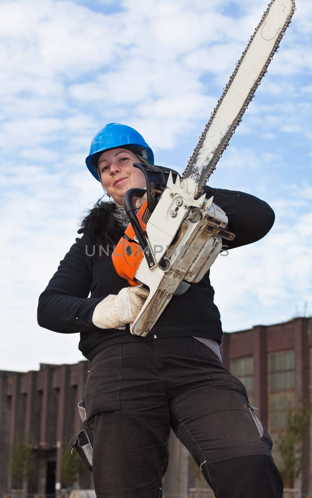 Female worker in workwear and hardhat holds large chainsaw