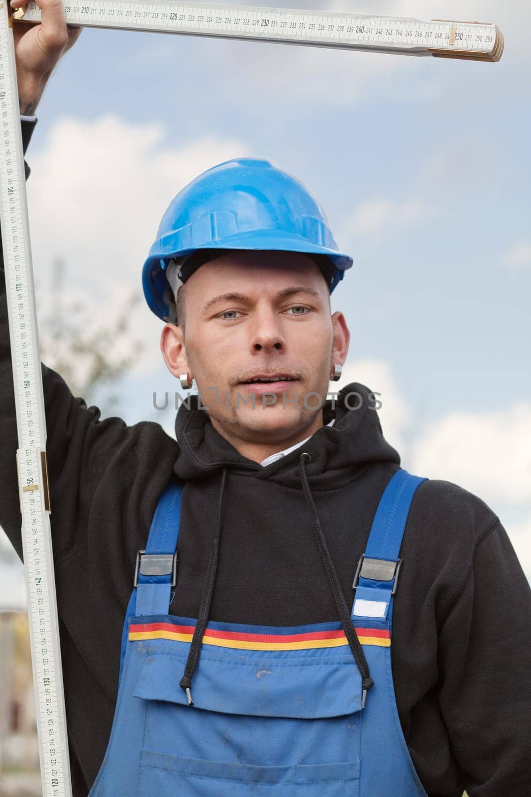 Manual worker in hard hat stands outdoor with foldable ruler