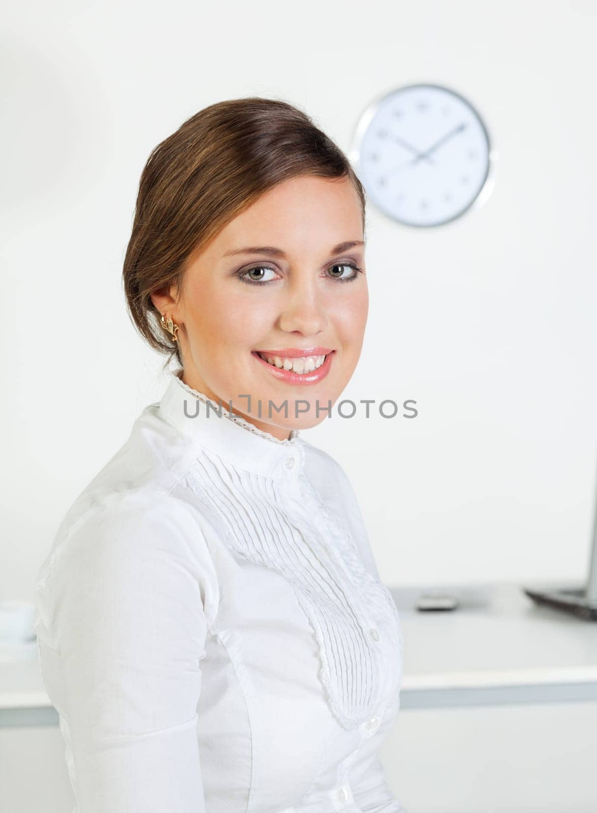 Young pretty smiling businesswoman standing in front of her desk in the office