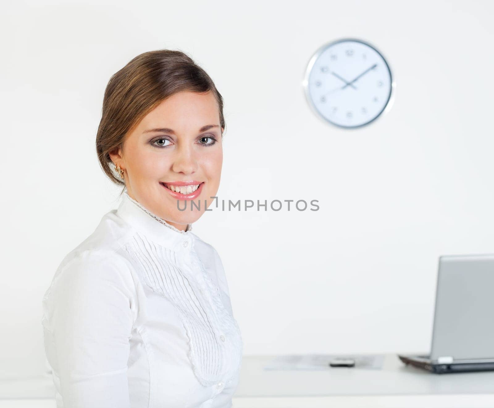 Young pretty smiling businesswoman standing in front of her desk in the office