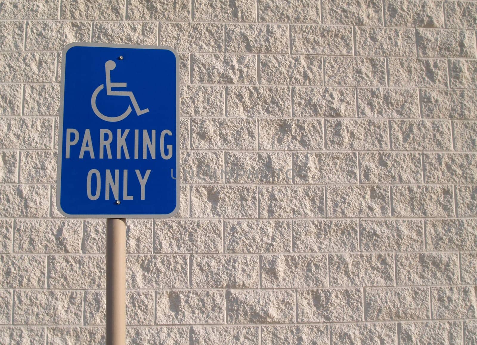 Blue handicap parking sign with a white textured concrete block background that can be used for copy space.