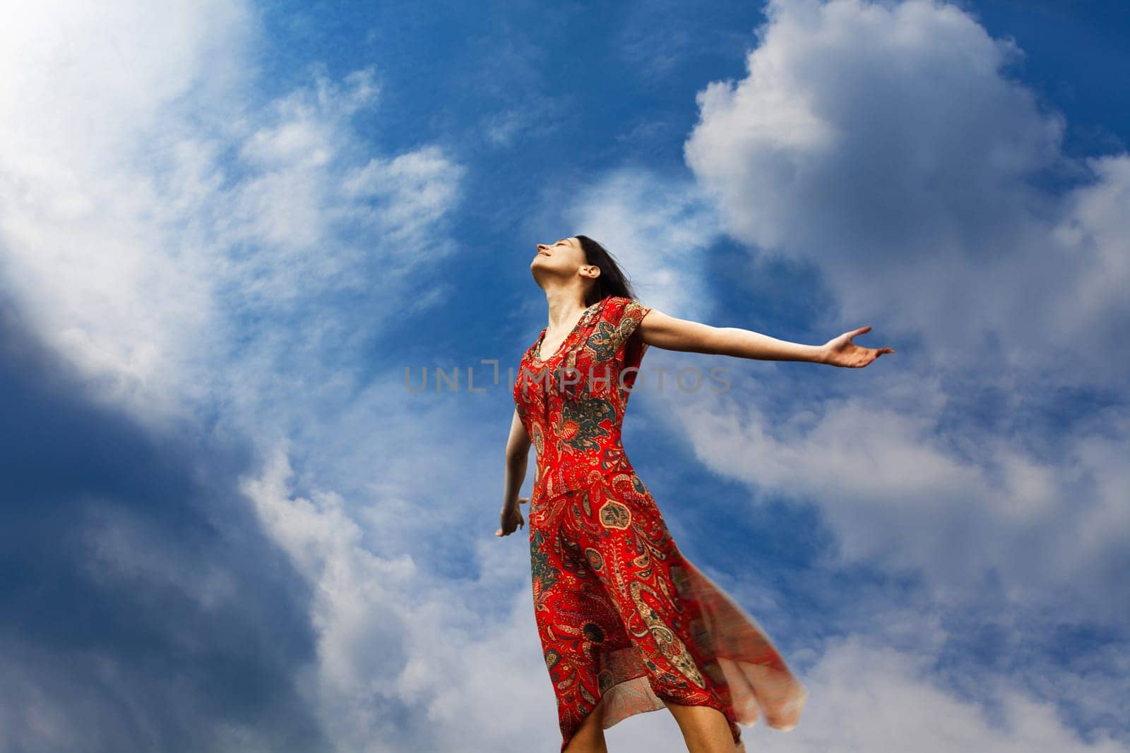 Pretty young woman with arms raised standing almost weightlessly towards the sun
