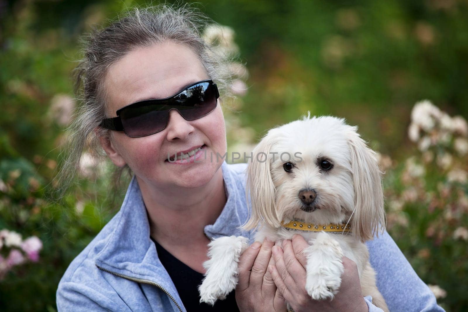 Middleaged woman holdiong her small dog and smiling at the cmaera.