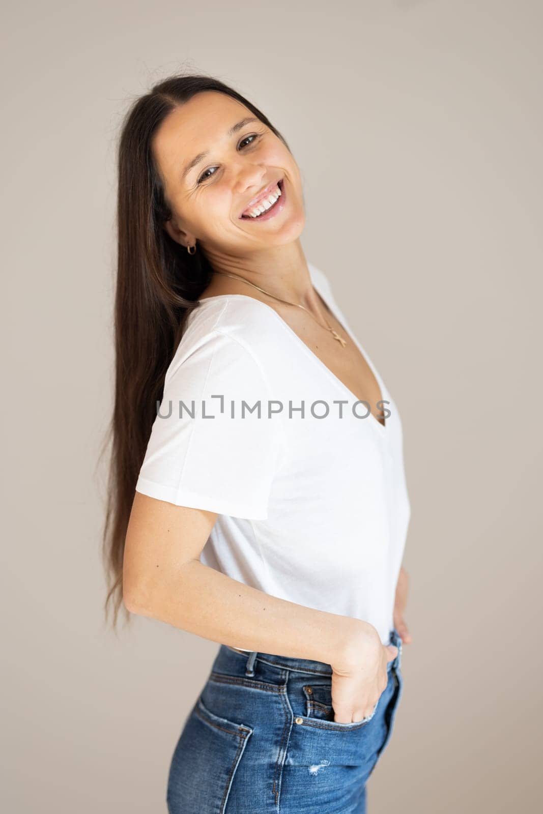 Portrait of confident beautiful woman with long brown hair, wearing casual clothes, standing in relaxed pose with hands in pockets, smiling with white teeth at camera, studio background. by kasto