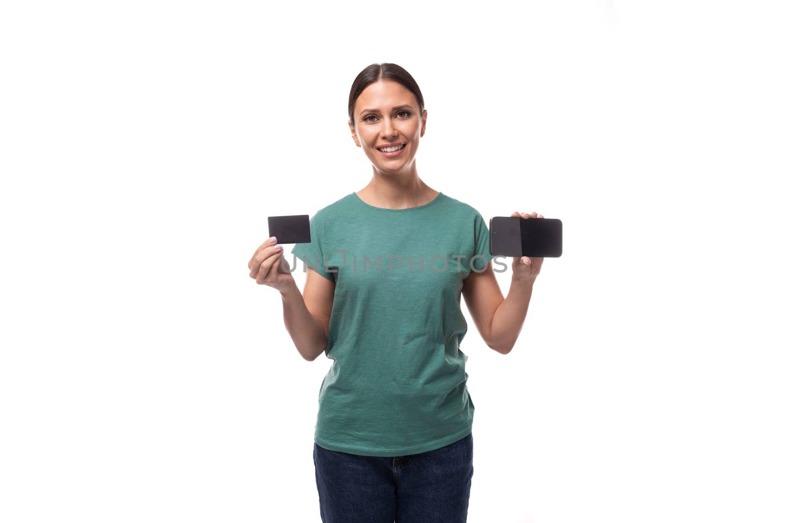 young joyful positive black-haired woman in a green basic t-shirt advertises a credit card and a smartphone.