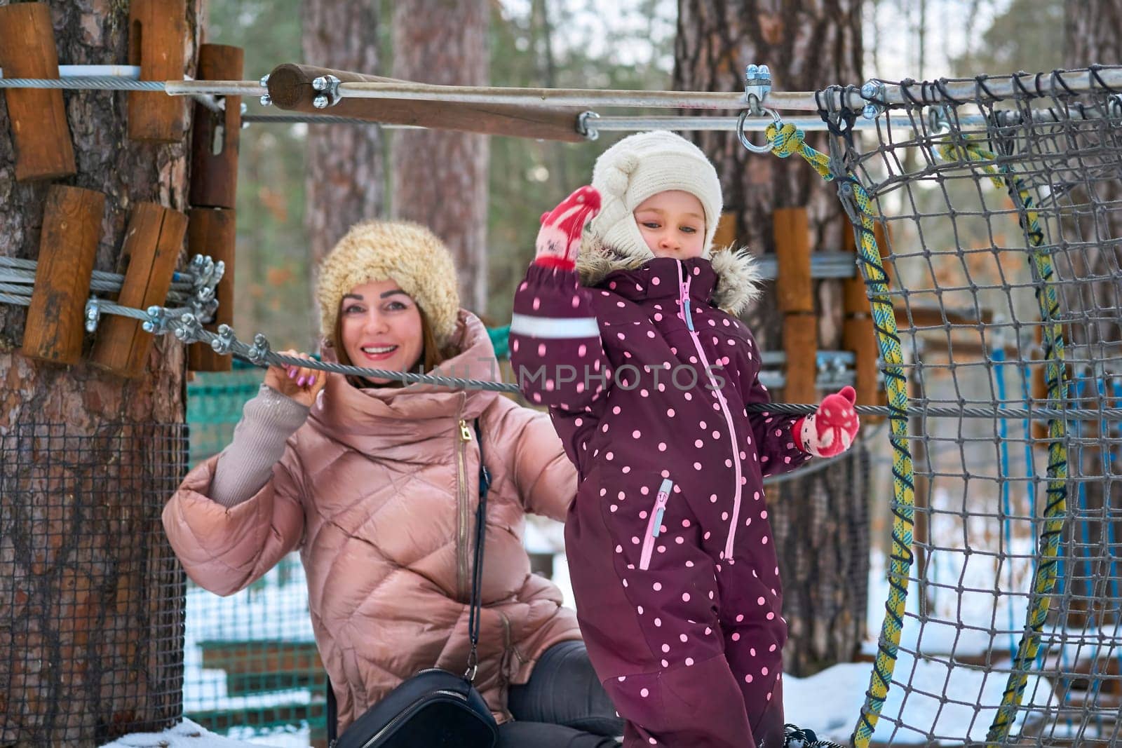 Cheerful mother with a child on a playing net stretched on trees in winter park by jovani68