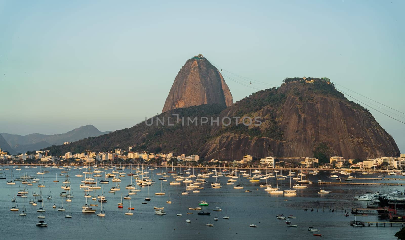 Iconic dusk scene of Sugarloaf Mountain & Morro da Urca with sailboats at Botafogo Bay in Rio de Janeiro, ideal for travel and tourism.