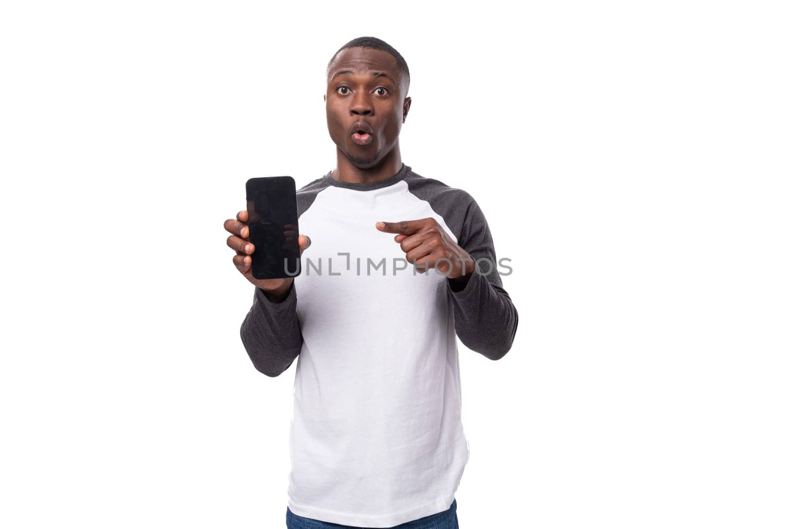 young american guy with short haircut dressed in a long-sleeve sweater reports the news pointing with his hand at a smartphone with a mock-up for advertising by TRMK