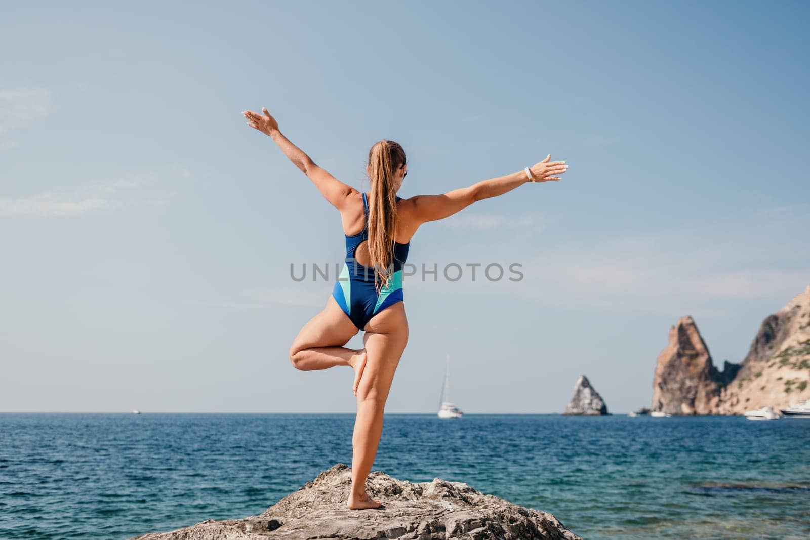 Woman sea yoga. Back view of free calm happy satisfied woman with long hair standing on top rock with yoga position against of sky by the sea. Healthy lifestyle outdoors in nature, fitness concept.