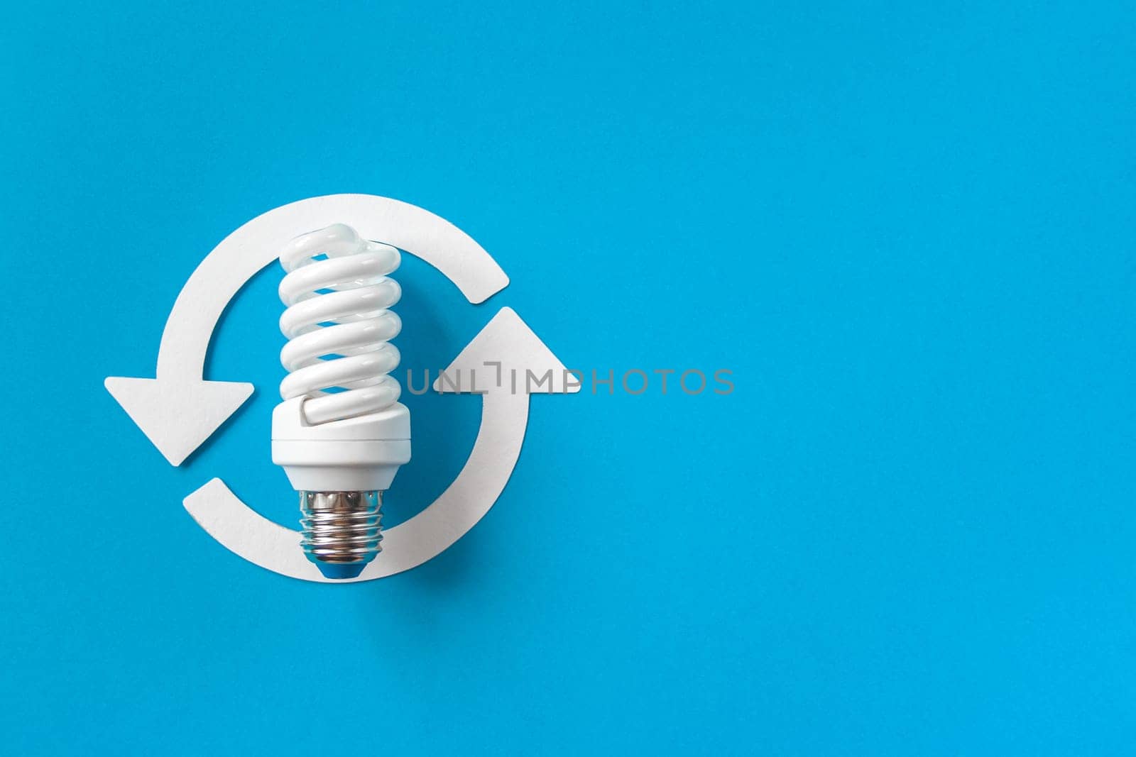Energy saving light bulb and recycle arrows. Economical consumption of electricity. Blue background copy space. The concept of nature conservation and renewable energy sources
