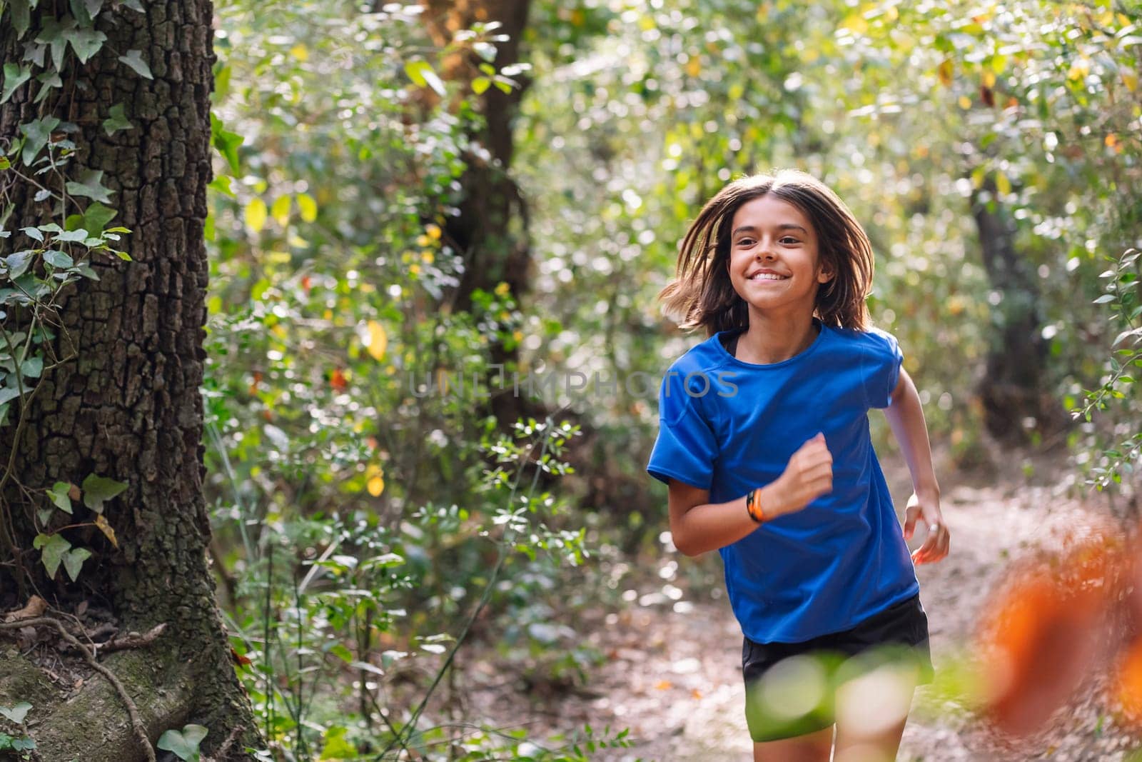 portrait of a smiling girl practicing trail running in the woods, concept of sport for children in nature and healthy lifestyle, copy space for text