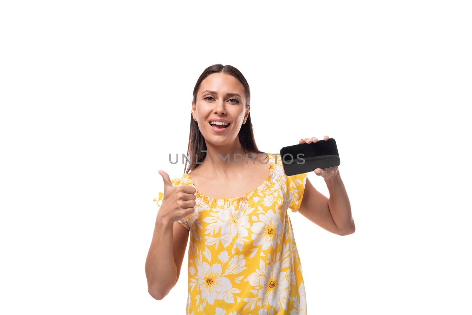 young pretty woman with straight black hair in a yellow sundress with a daisy pattern shows a smartphone screen with a mockup.