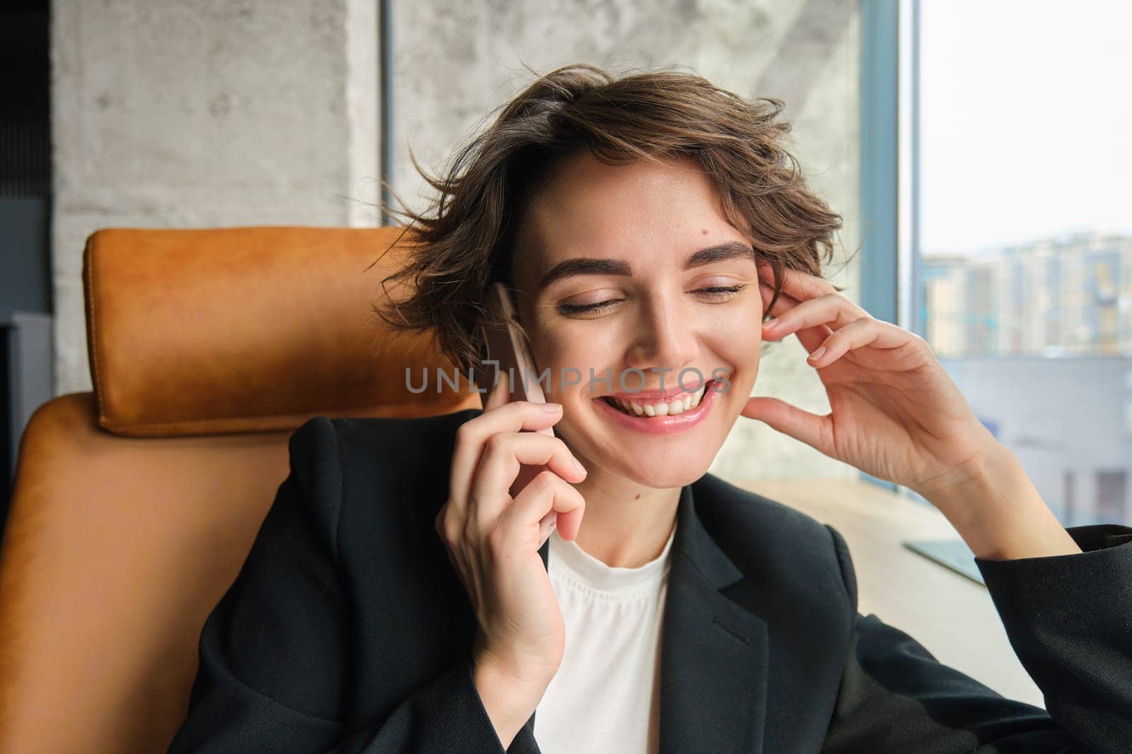 Close up portrait of corporate woman laughing and smiling, talking over the phone, sitting in office.