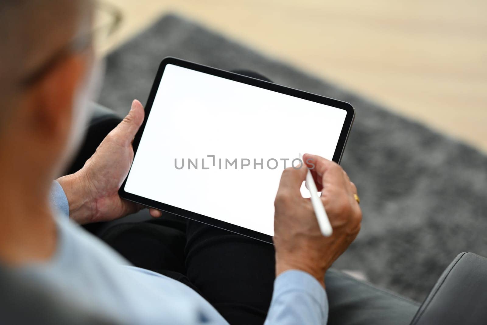 Over shoulder mature man using stylus pen writing on digital tablet. Elderly lifestyle and technology concept.