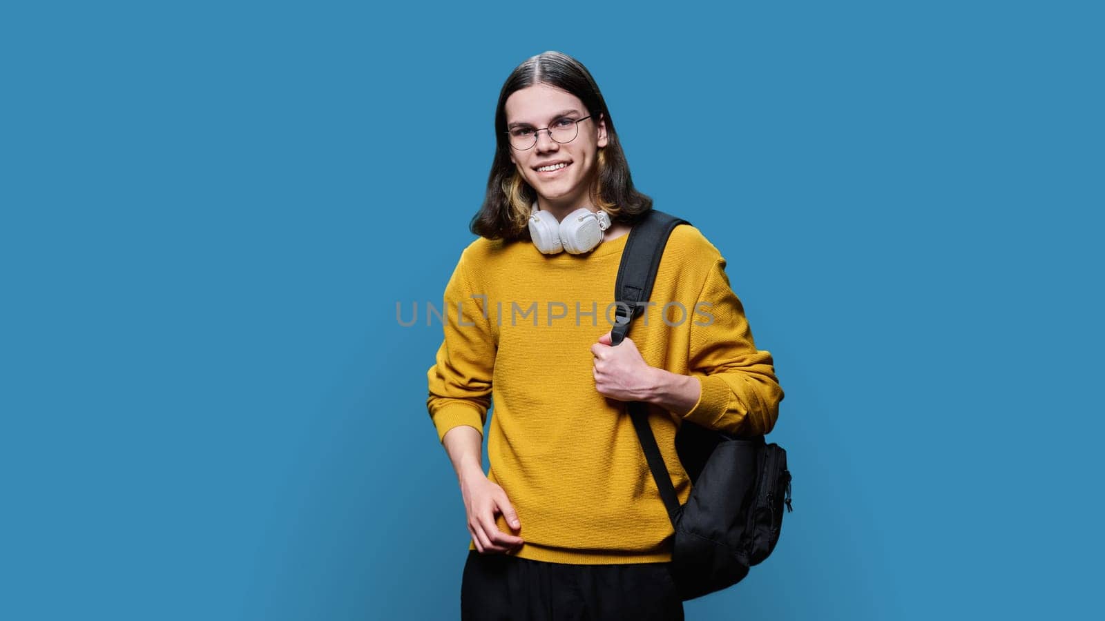 Portrait of university student guy on blue studio background. Smiling handsome young male with backpack looking at camera. College, university, education, knowledge, youth concept