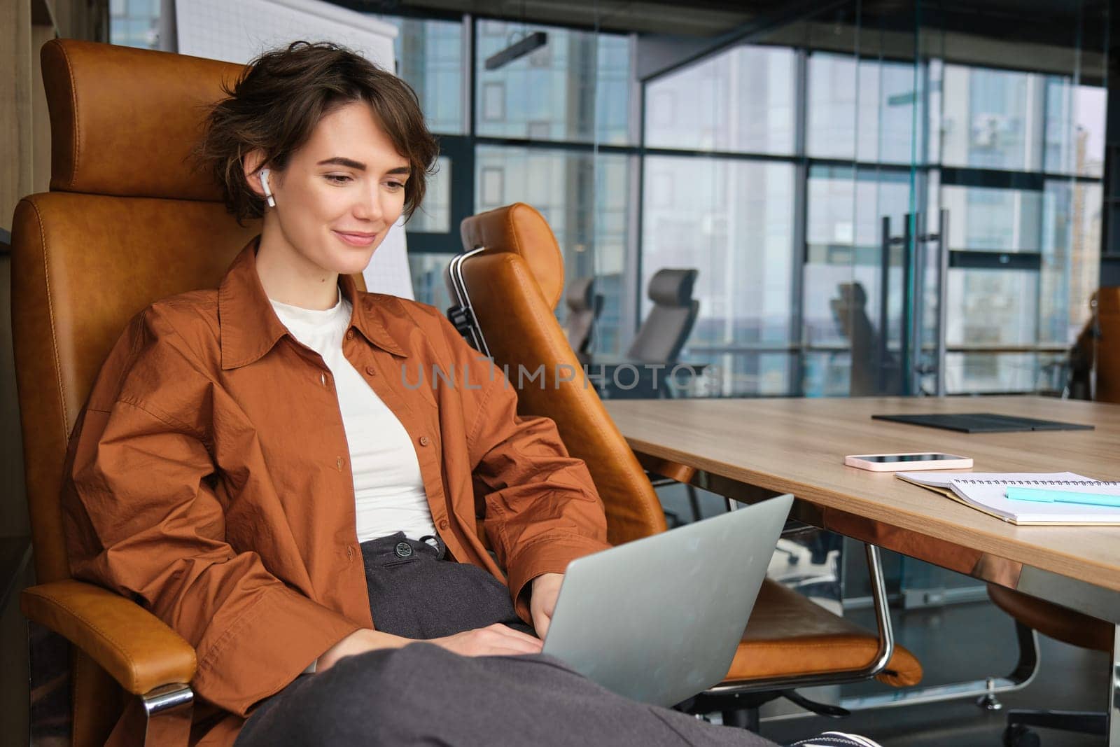 Portrait of smiling young woman, manager works in office, uses laptop, works from co-working space.