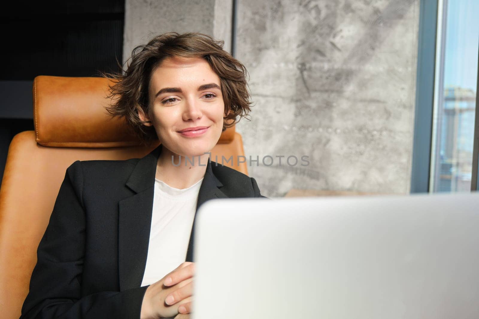 Portrait of young successful businesswoman giving presentation online, attending webinar on laptop, sitting in office, looking at computer screen. Corporate people and business concept