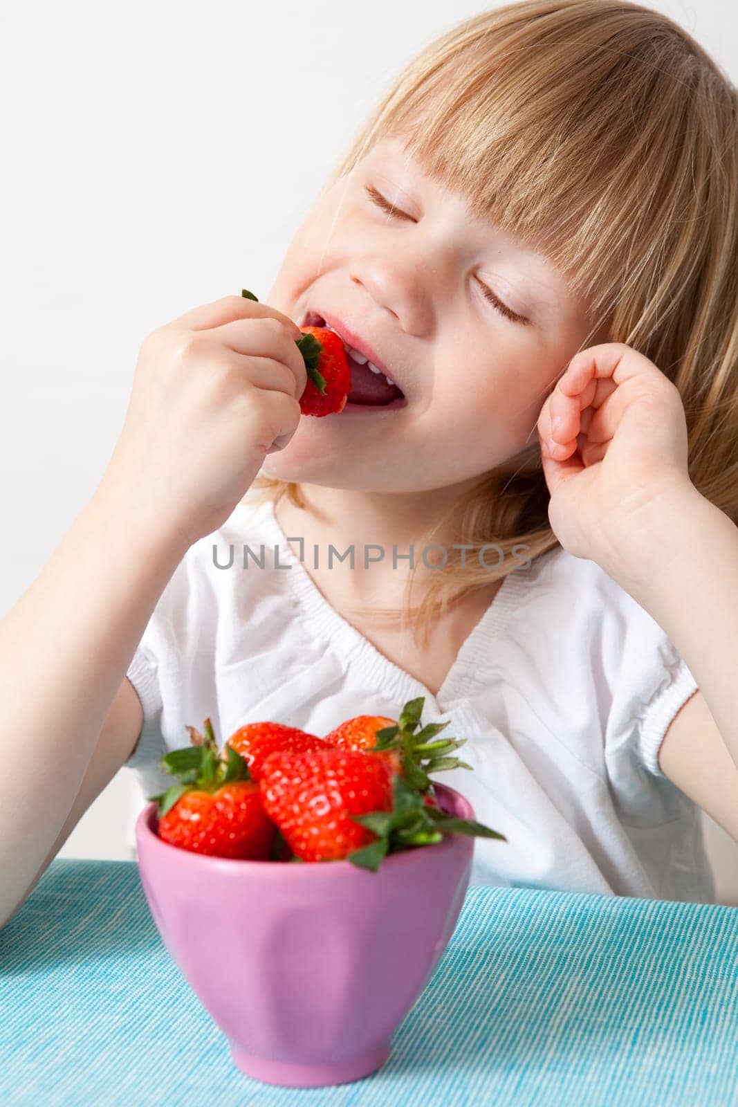 Little girl eating delicious ripe strawberries, bowl in front of her.