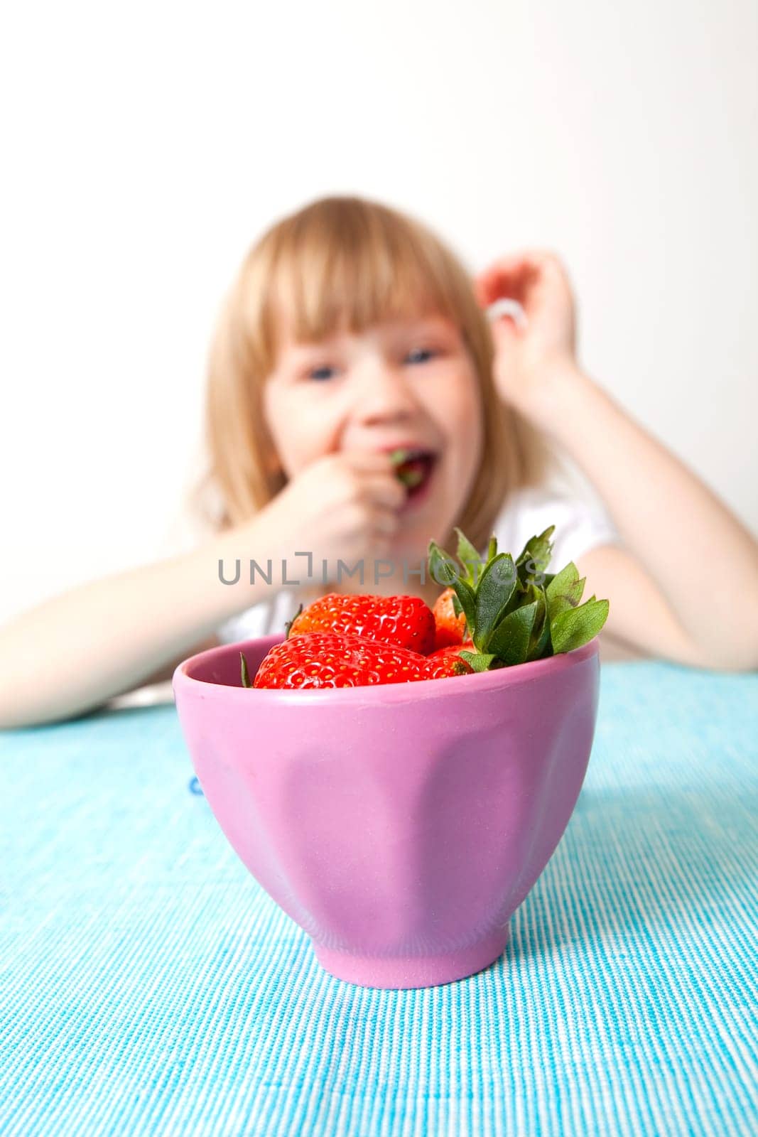 Little girl eating delicious ripe strawberries, bowl in front of her.
