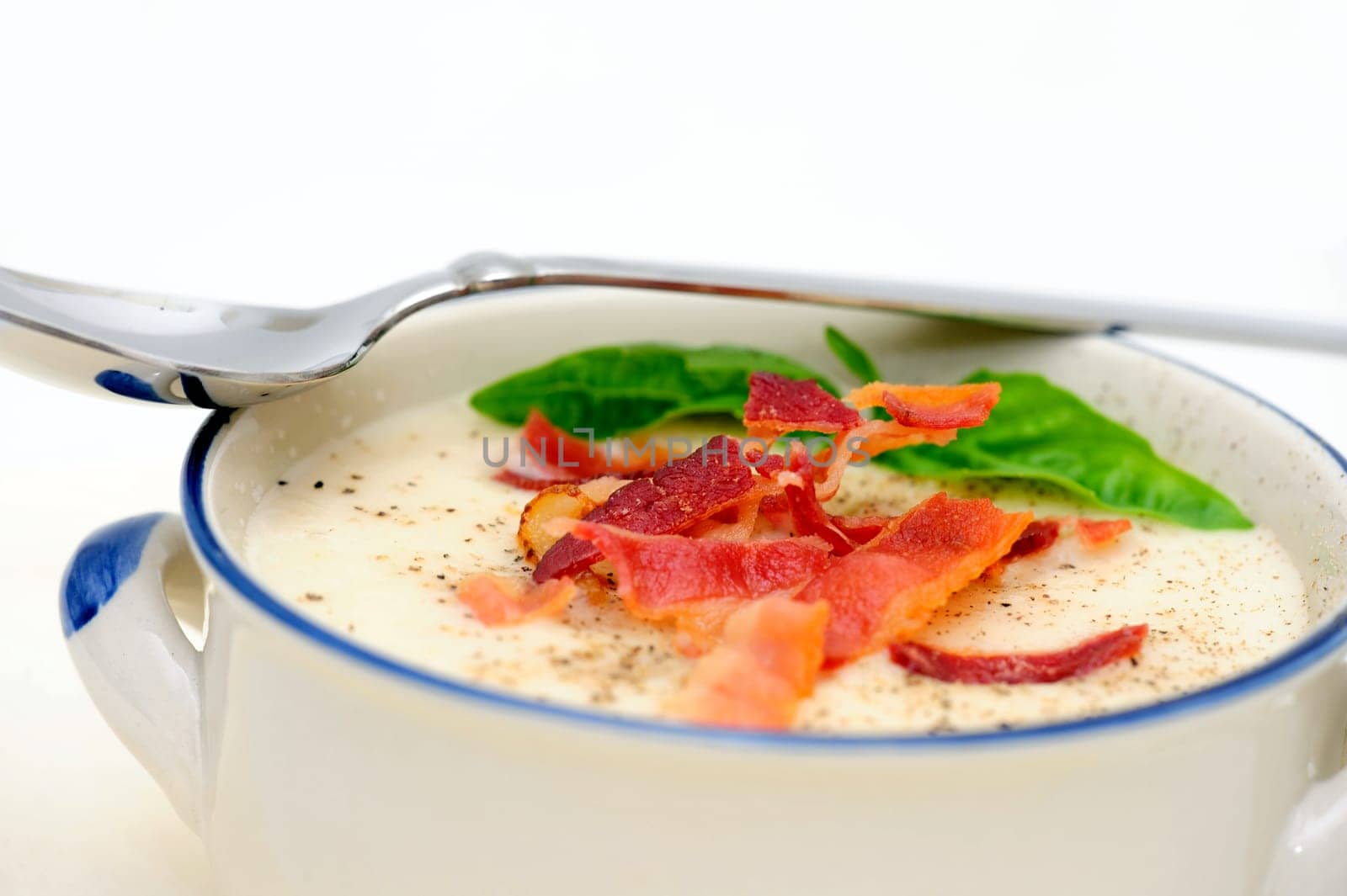 Potato soup topped with crisp bacon and fresh Basil leaves served in a rustic blue and white bowl