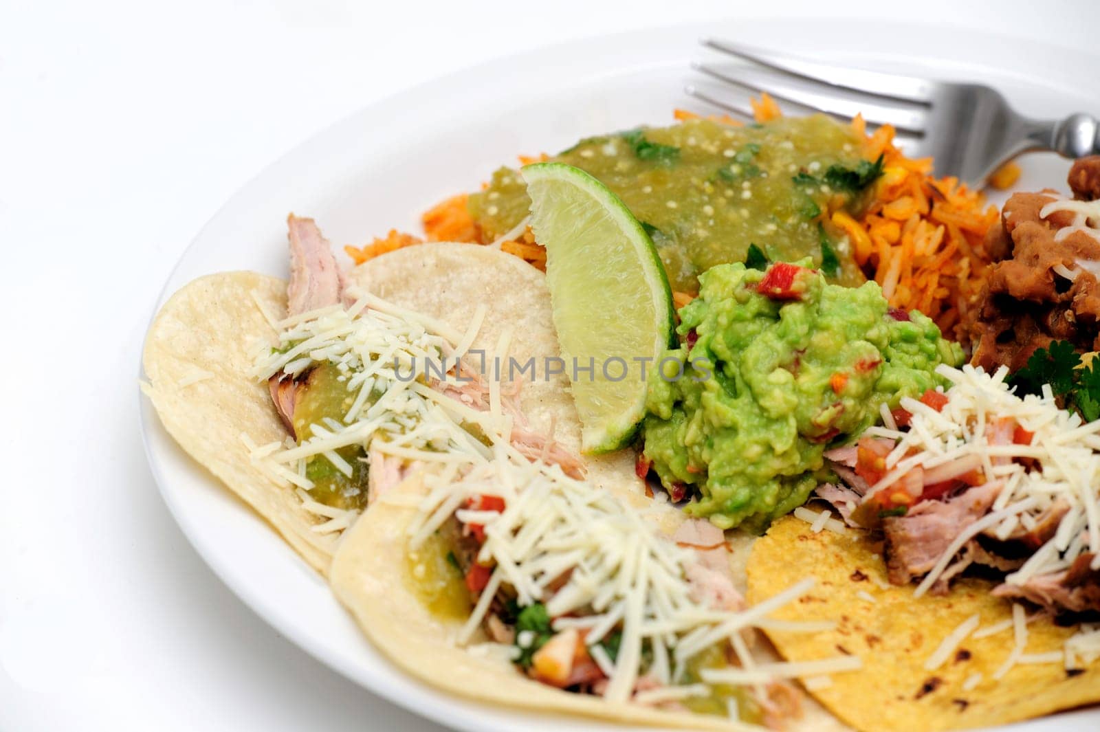 Mexican style meal of Pork Carnitas soft tacos with refried beans, Spanish rice topped with fresh salsa verde and spicy guacamole.