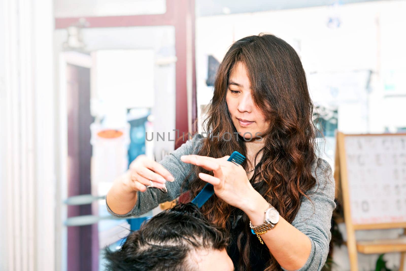 Happy hairdresser cutting hair in her salon
