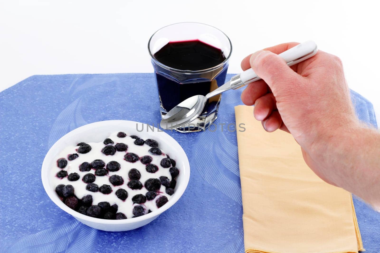 Man&#039 s hand with spoon ready to eat bowl of yogurt with blueberries, and drink blueberry juice.