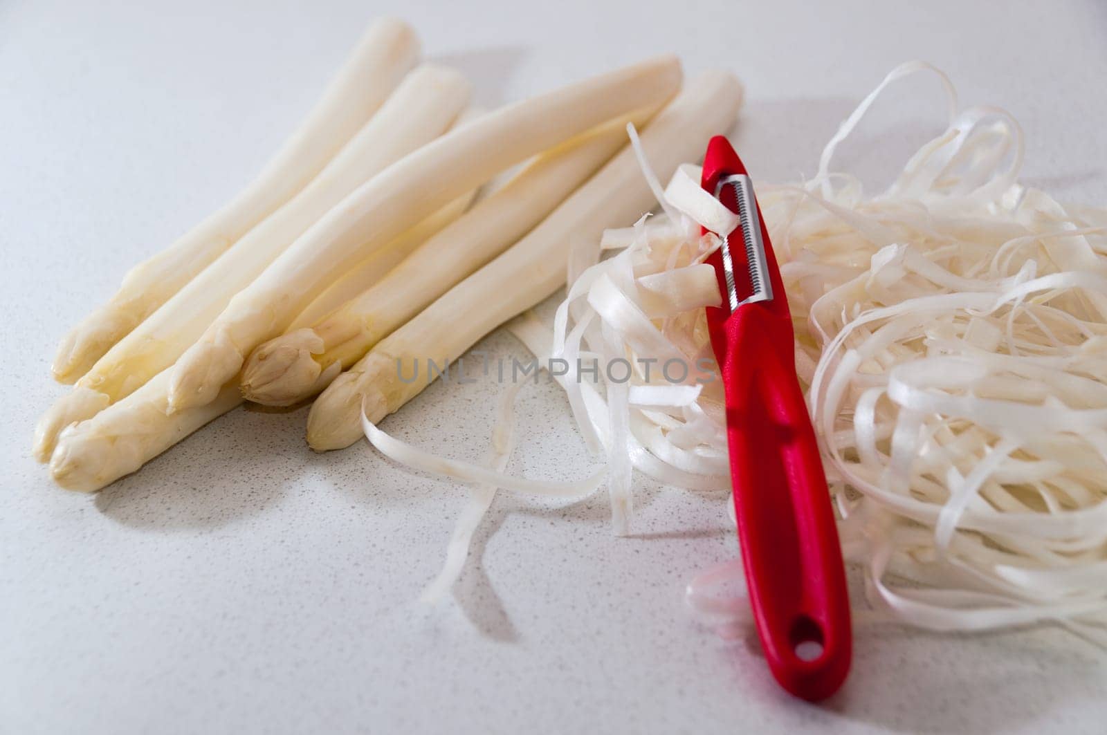 Wite asparagus with red peeler in kitchen