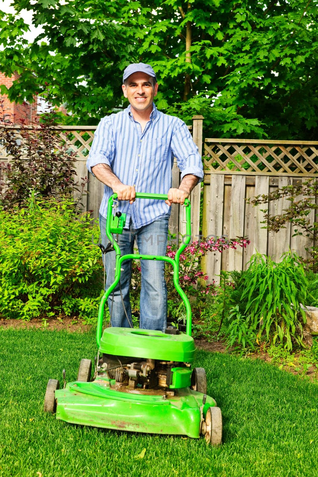 Man with lawn mower in landscaped backyard