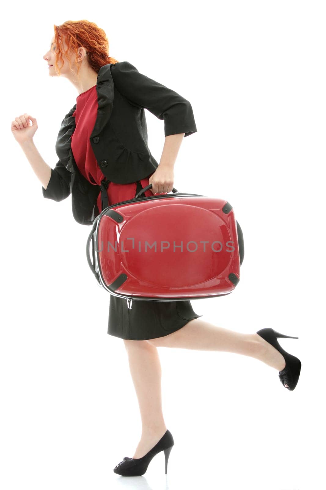 Young redhead businesswoman (deaf with hearing aid) with red suitcase, isolated on white background