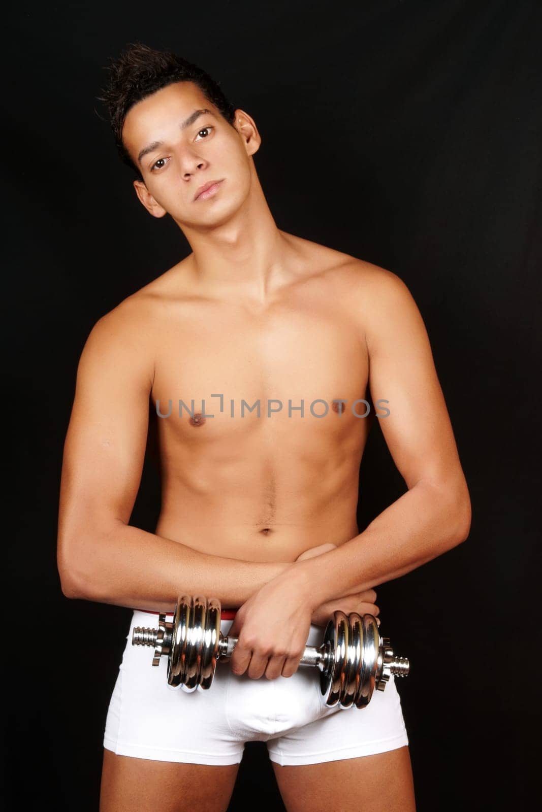 Smiling young man in underwear training with a chrome dumbbell