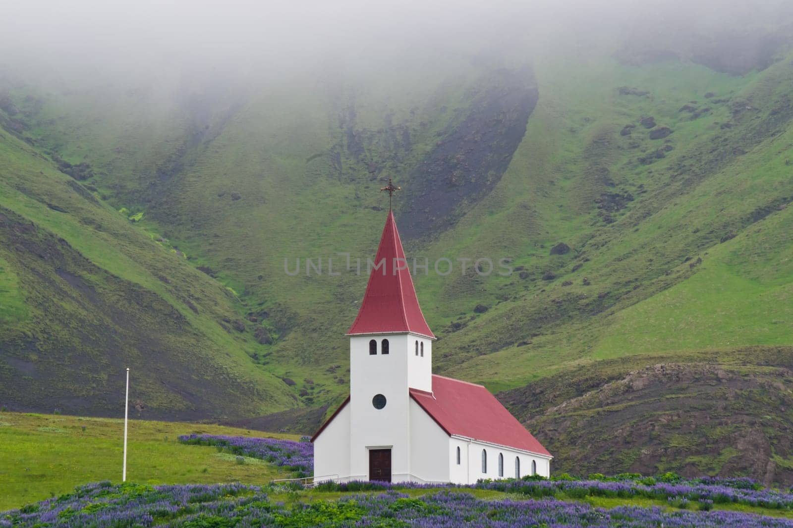A little church in the south of Iceland surrounded by hills and green meadow on a foggy day.