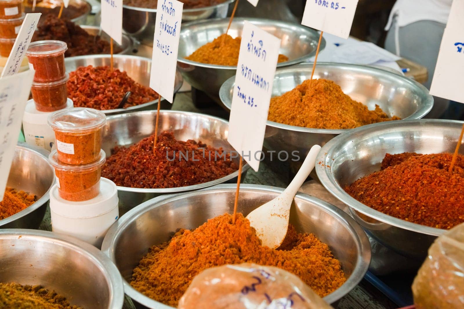 Different red and yellow colored curry paste in large bowls for offer at a market in Thailand.