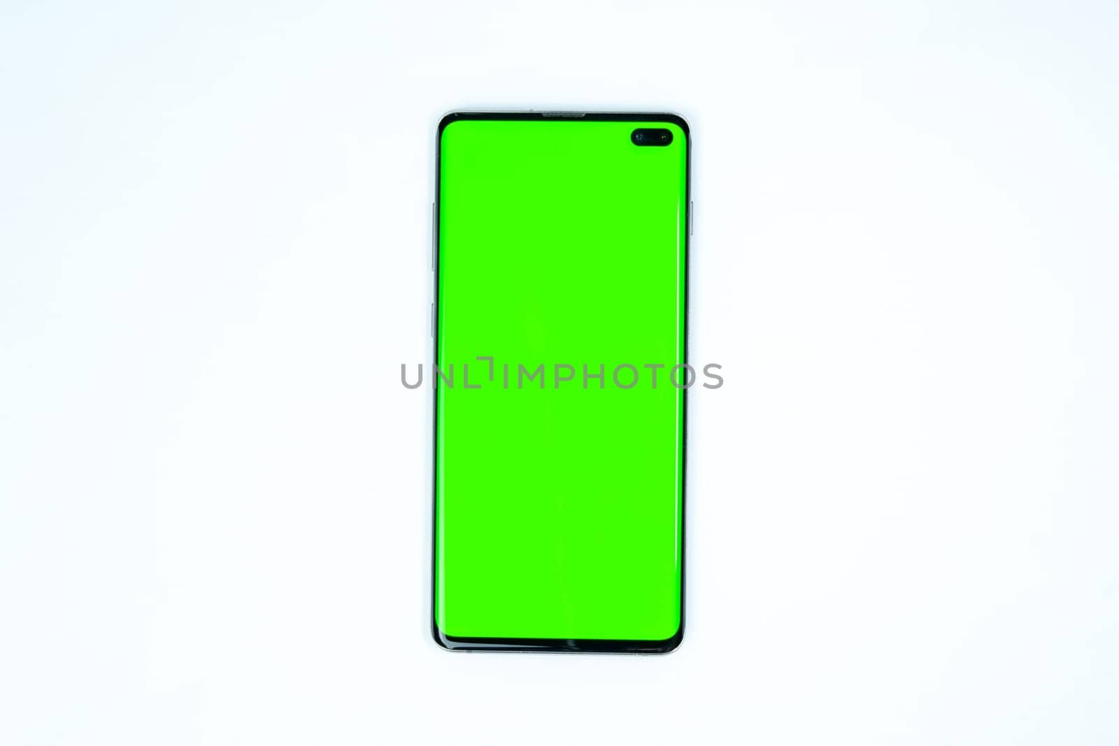 Modern smartphone with a bright green screen placed on a wireless charging pad, isolated on a white background, suitable for mockups and design presentations.