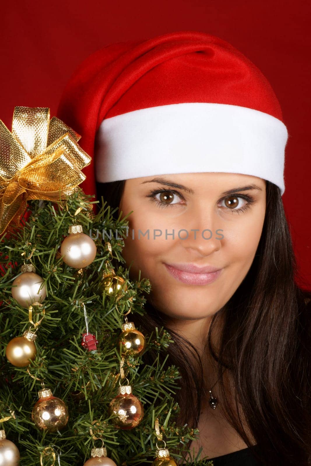 Beautiful 18 years old Santa Claus girl with Christmas tree over a red background