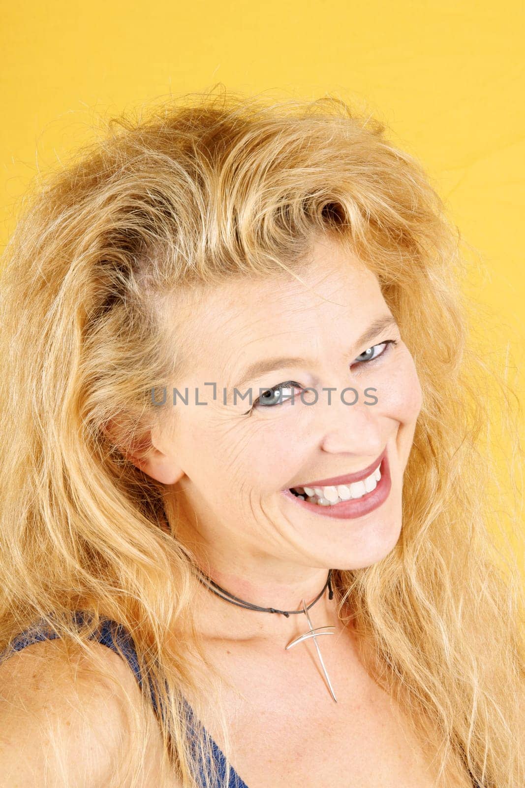 Portrait of a smiling beautiful blond lady in her 40s. Over a yellow background.