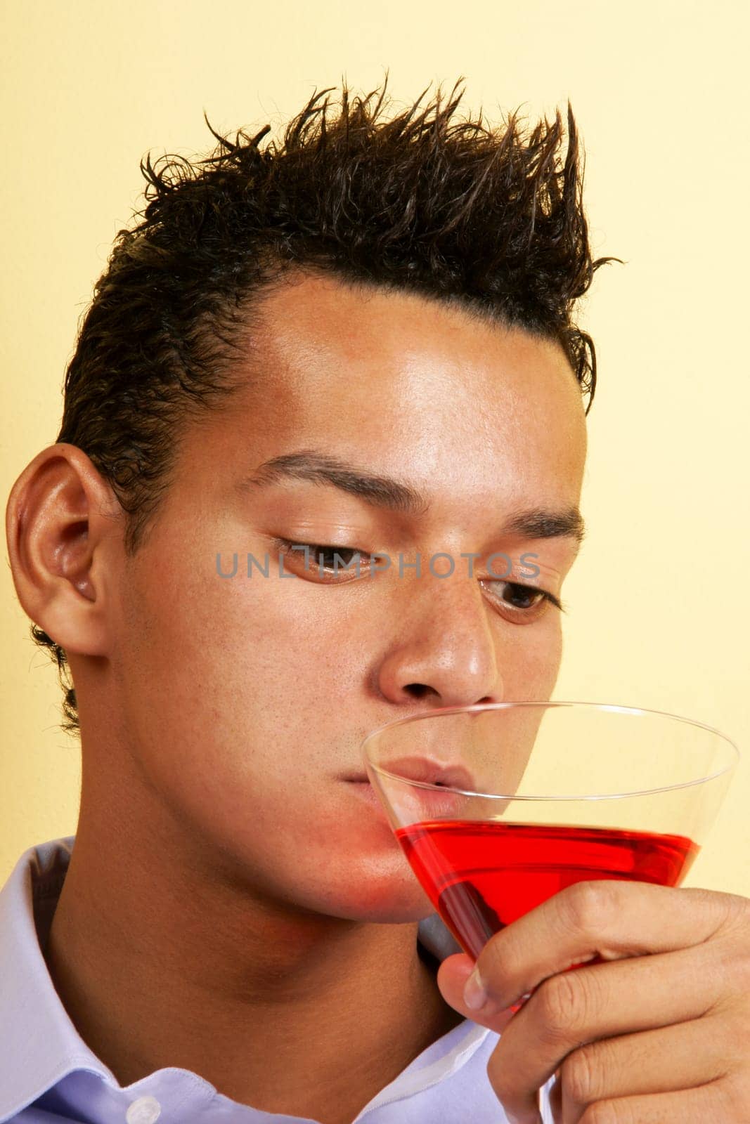 Sad young man drinking red cocktail from a martini glass.