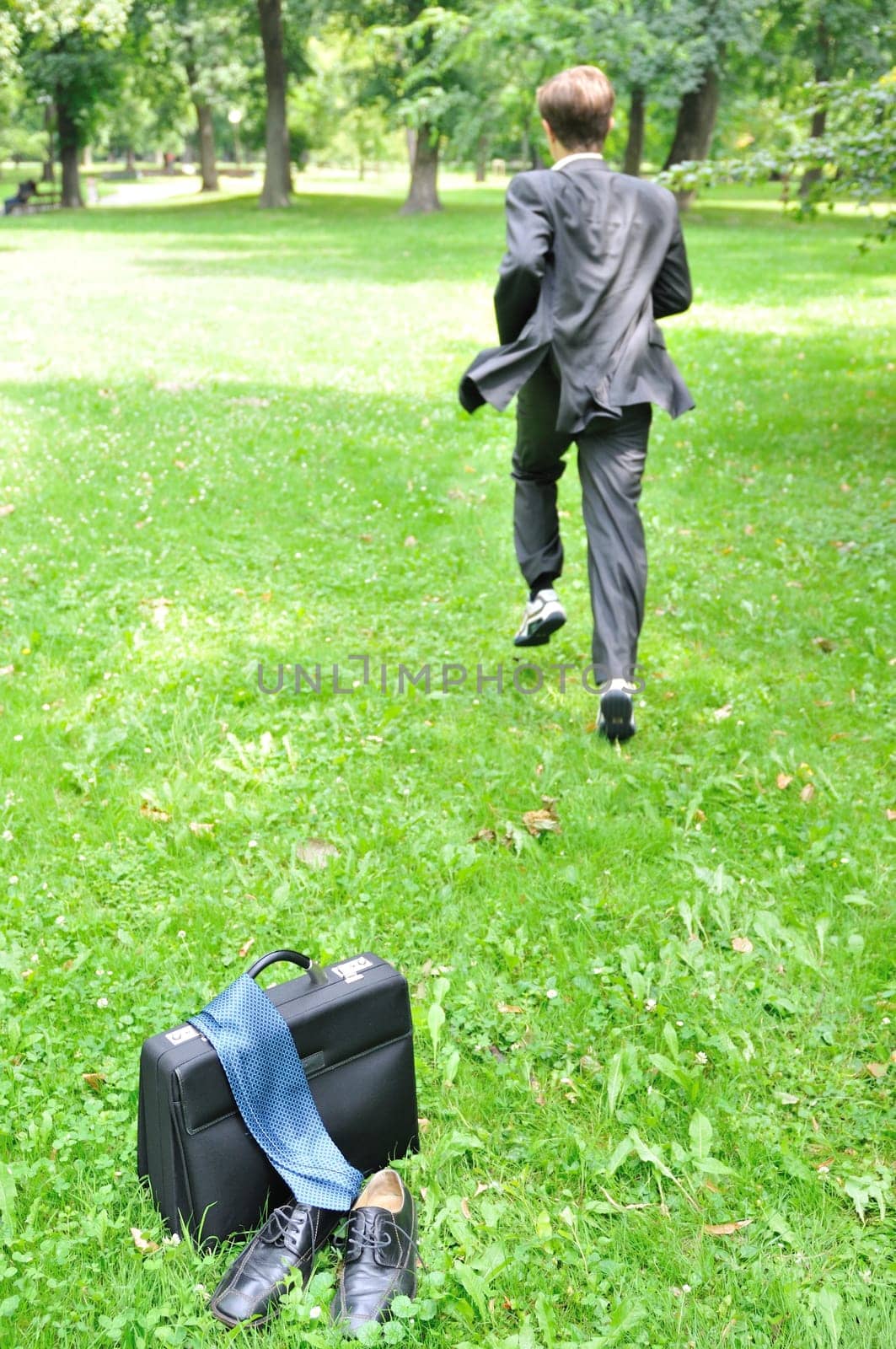 Escape from civilization concept - business man running in park away from bag, shoes and tie