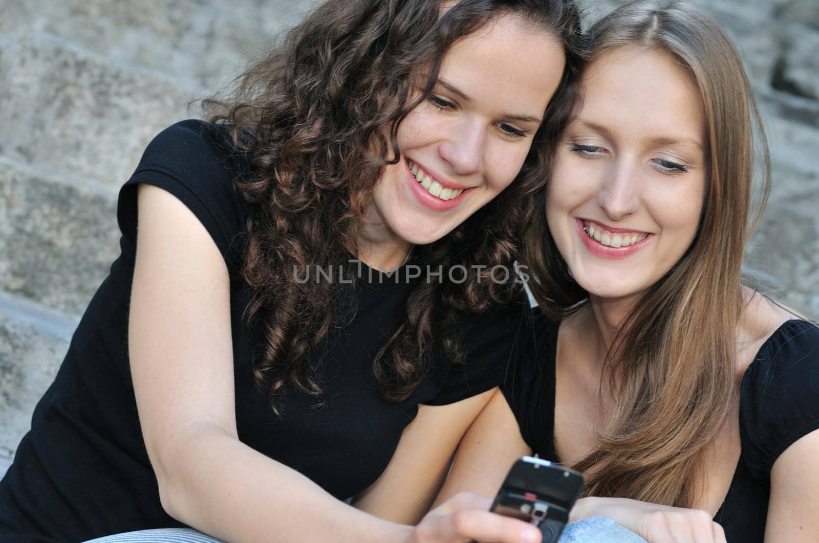 Youth lifestyle - two smiling friends (girls) outdoors with mobile phone