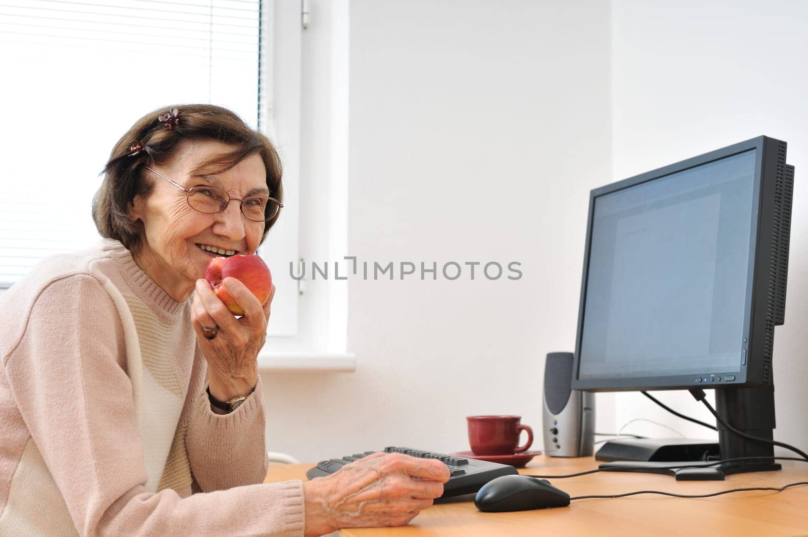 Portrait of smiling mature woman sitting at computer eating apple