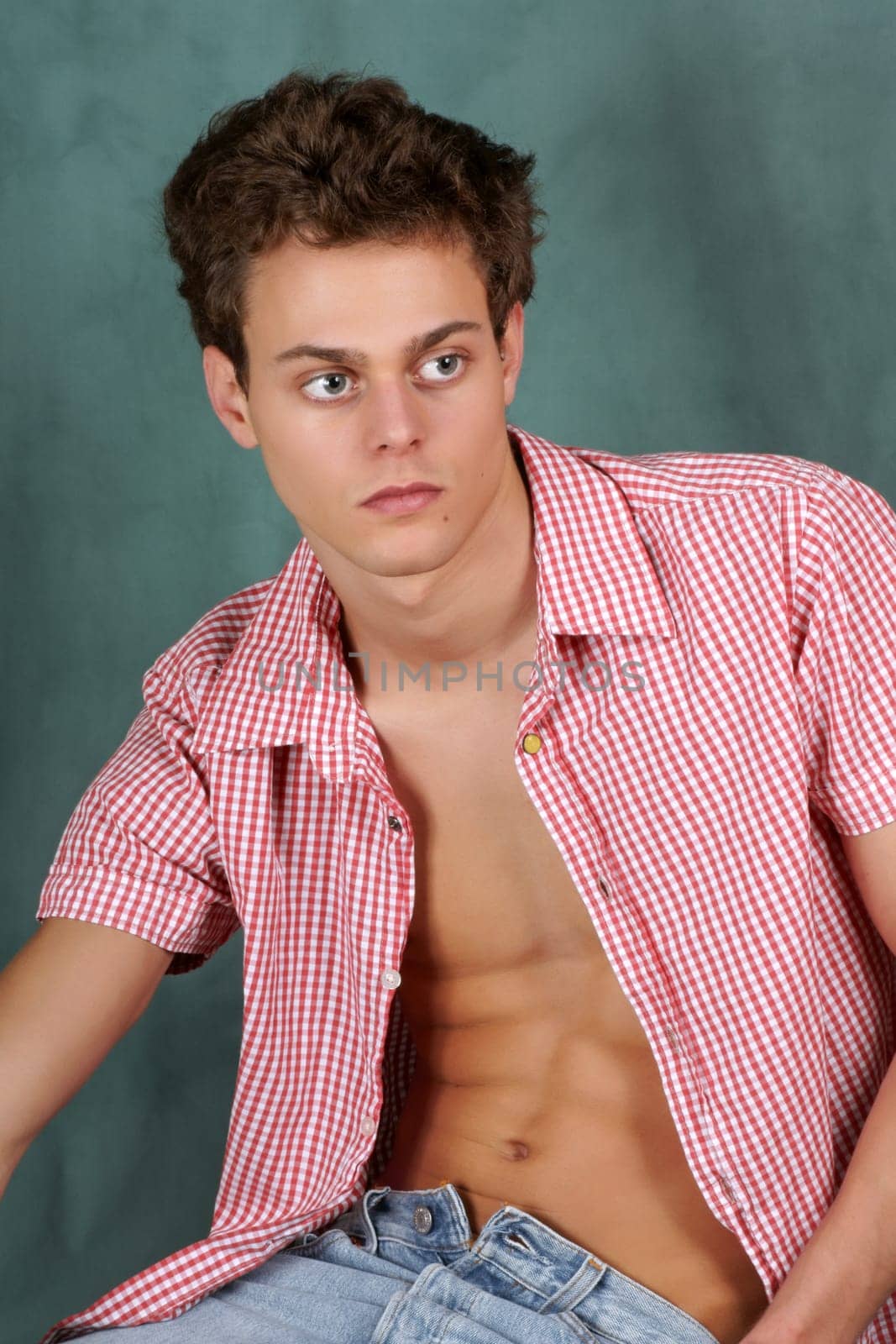 Portrait of a young man with unbuttoned chequered shirt over a green background