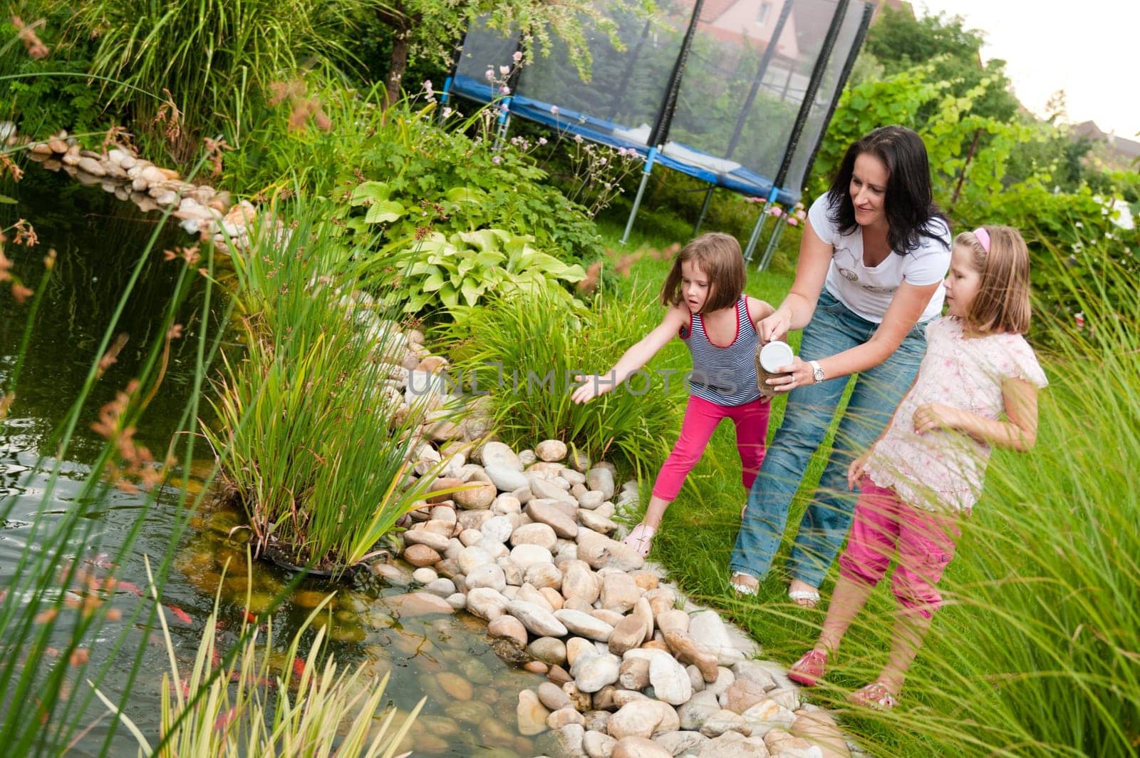 Family (mother and two children) feeding fish in garden pond