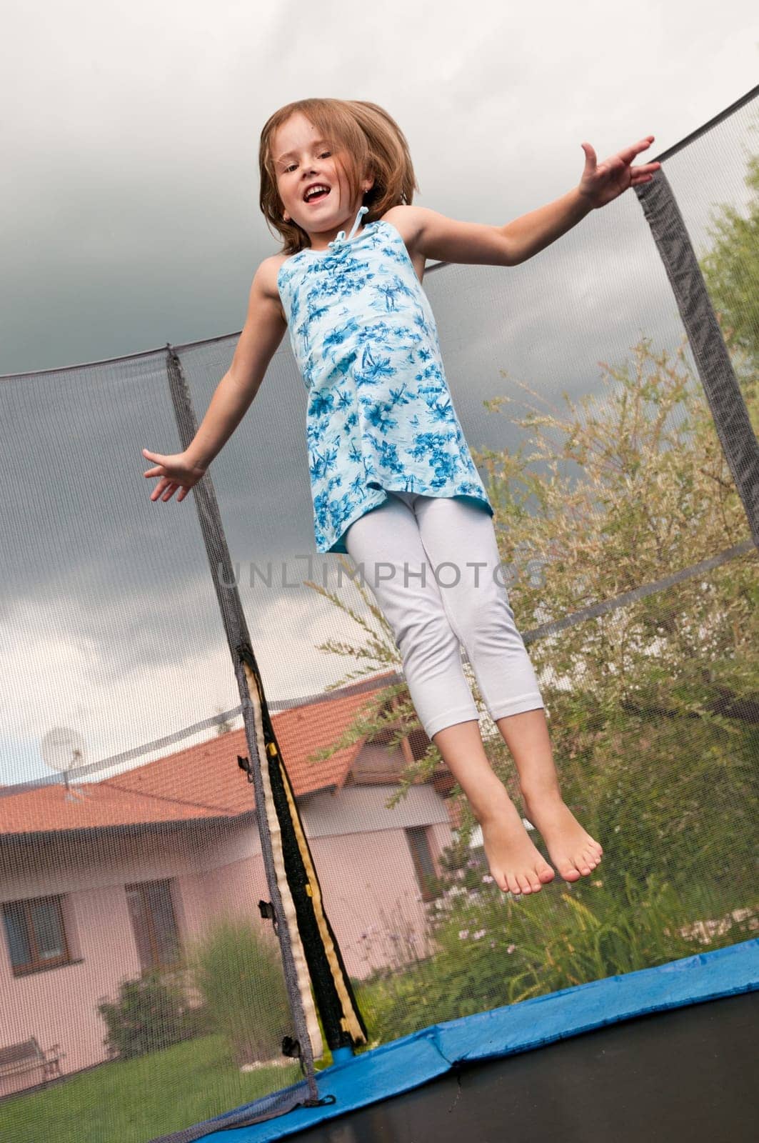 Small cute child jumping on trampoline - garden and family house in background