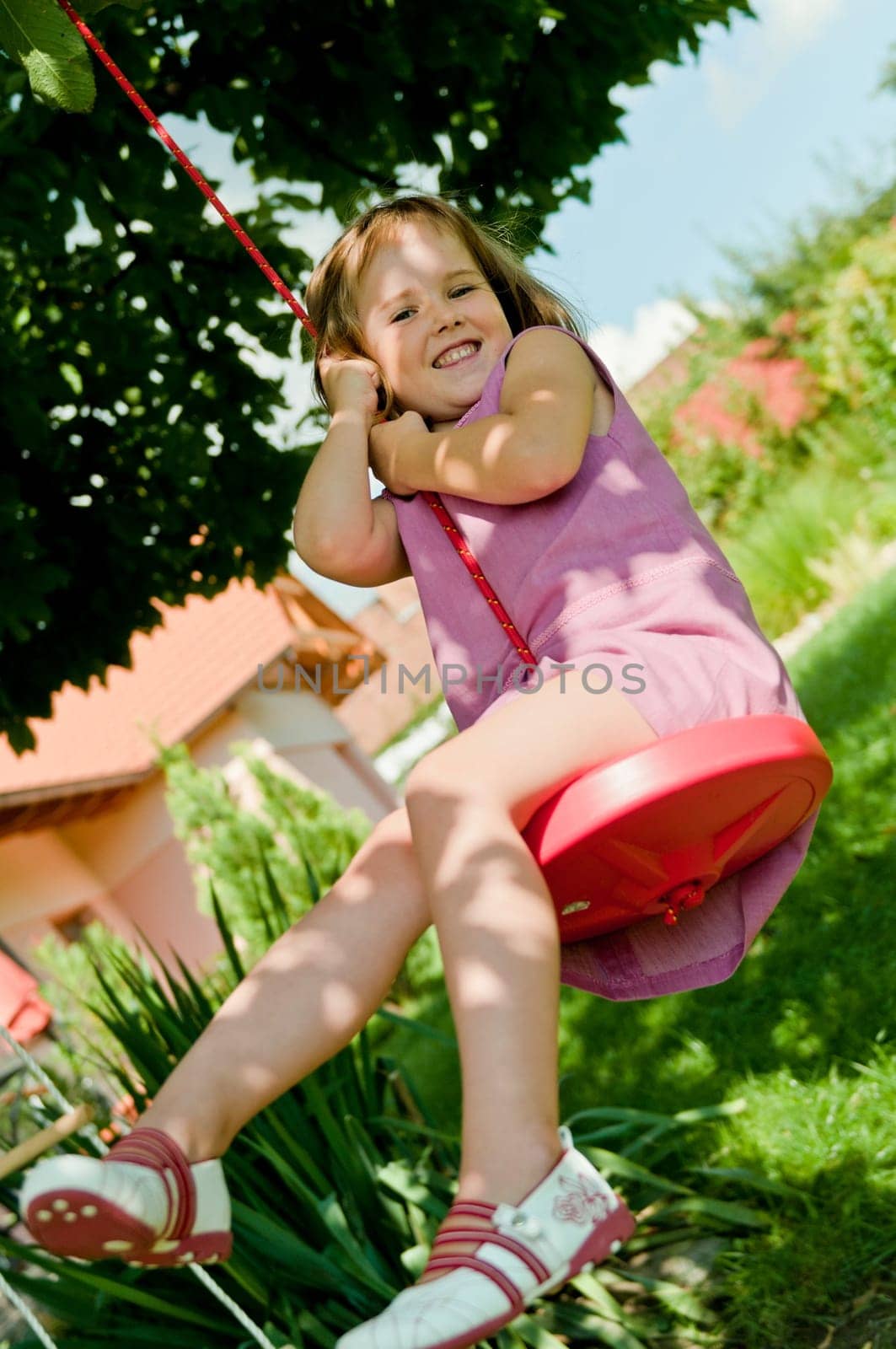 Happy small cute girl swinging on seesaw in garden behind family house