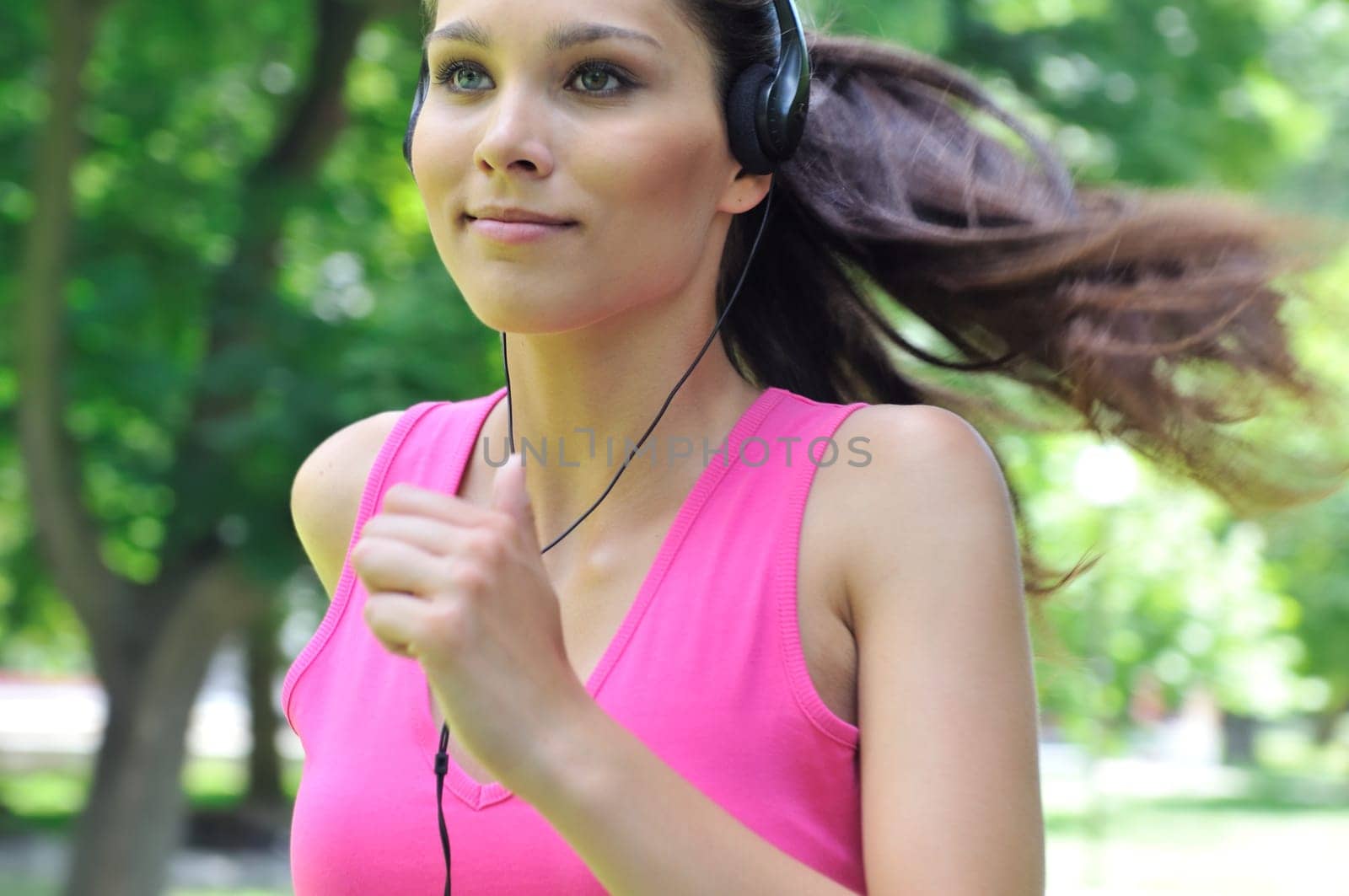 Young person (woman) with headphones listening music running outdoors in park on sunny day