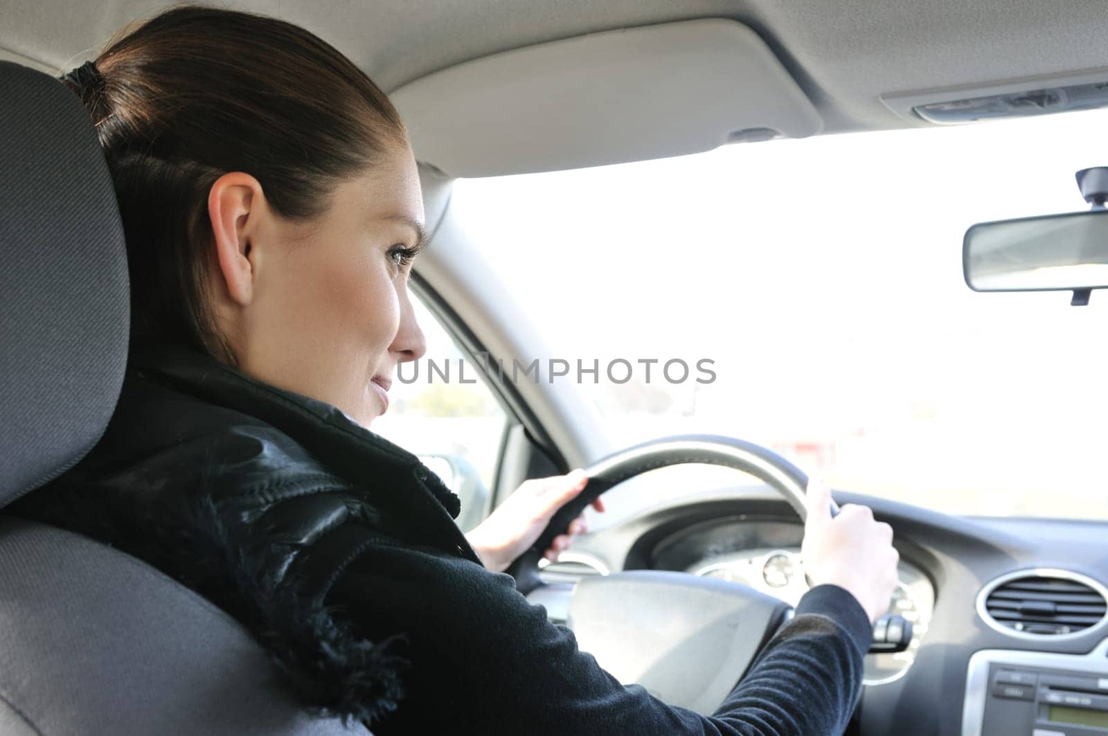 Lifestyle shot of young cheerful woman driving car - rear view